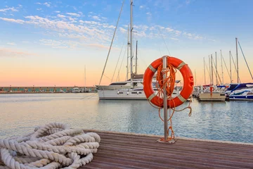 Fotobehang the quay of a marina at  the sunset /a mooring rope with a lifebelt  on  the quay of a marina at  the sunset © cannes106