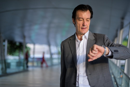 Mature handsome businessman checking time from wrist watch outdoors