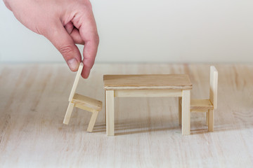 A hand putting a miniature chair to a dining table, interior design or apartment furnishing concept, invitation to have a seat at the table together
