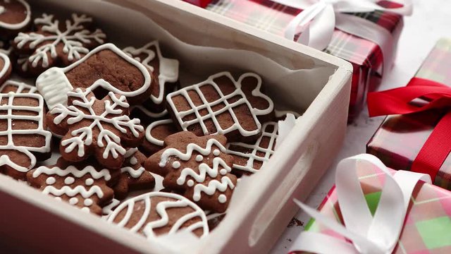 Delicious fresh Christmas decorated gingerbread cookies placed in wooden crate. Wrapped gifts on sides. White rusty background. Top view.