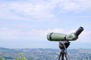 Green spotting scope or monocular at mountain top against the background of a mountain landscape in...