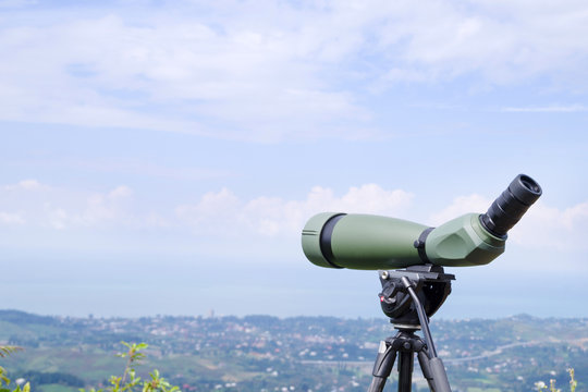 Green spotting scope or monocular at mountain top against the background of a mountain landscape in summer day. Observation of birds, birdwatching