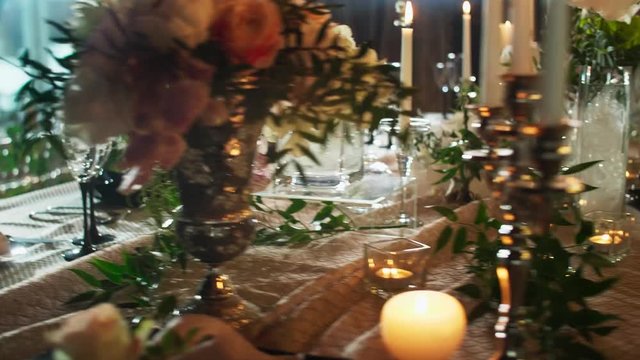 a row of wine glasses on a table served with black plates, candlesticks with candles and flower vases