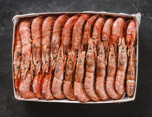 Fresh red shrimps or prawn packing in box on slate stone background. Seafood, top view, flat lay, copy space