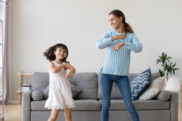 Cheerful mother little daughter standing in living room at home moving dancing to favourite song together. Child have fun with elder sister nanny or loving mother active leisure and lifestyle concept - obrazy, fototapety, plakaty