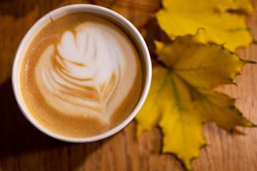 cup of cappuccino with leaves on table
