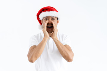 Positive Asian man cupping hands around mouth and shouting loud. Guy wearing Santa hat. Christmas offer concept. Isolated front view on white background.