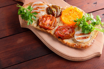 Toast with grilled vegetables. Vegetarian food. Red and yellow tomatoes. Grilled sandwich with tomatoes, onions and herbs. Bread with vegetables and honey. Vegan toast on wooden board