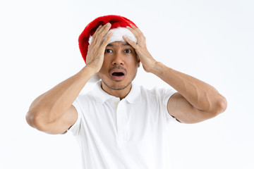 Stressed man wearing Santa Claus hat and clutching head. Worried Asian guy looking at camera. Christmas eve and problem concept. Isolated front view on white background.