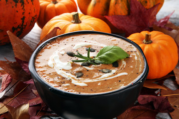 Roasted pumpkin and carrot soup with cream and pumpkin seeds on wooden background.