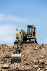 Yellow construction digger, excavator on demolition site stand on debris, sunny day clear blue sky