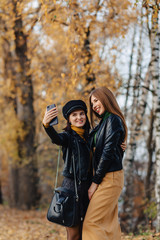 two cozy young girls walk at autumn park road an make photos