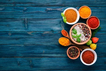 Tuinposter Spices and herbs on a blue wooden table. Basil, pepper, saffron, spices. Indian traditional cuisine. Top view. Free copy space. © Yaruniv-Studio