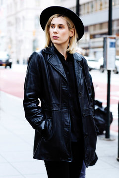 Portrait of a young woman with blonde hair and black hat, standing outdoors
