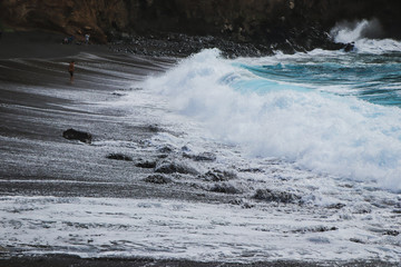 Sea waves hitting a beach with black volcanic sand with turquoise sea water. Seascape in the Portuguese coastline. Azores islands.