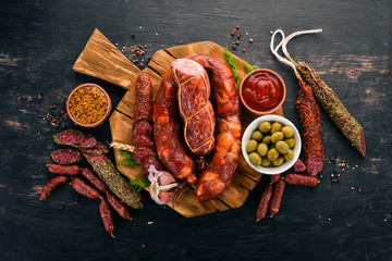 Sausage Fuet, salami, paperboard on the kitchen board. On a black background. Top view. Free space for your text.