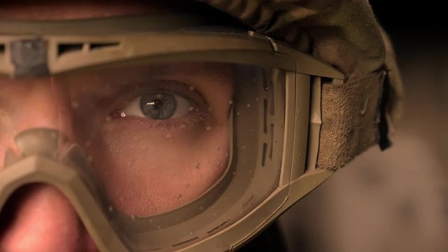 Close-up focused eye of strong military man in uniform and helmet, looking at camera while standing, authentic modern appearance
