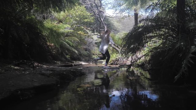 Young Woman Jumps Over Creek in Forest