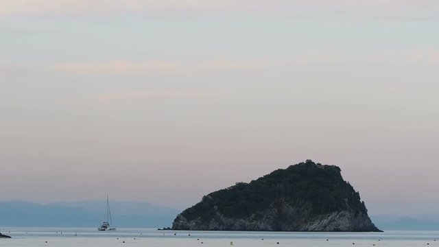 Spotorno, Bergeggi Italy_June 15,2018: catamaran sailboat anchored next to small island  viewed from Spotorno beach at sunset