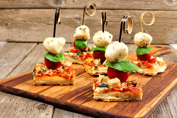 Caprese pizza skewers with mozzarella, basil, and tomatoes. Appetizers against a rustic wood...