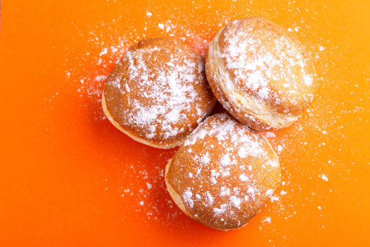Tasty sweet donuts with powdered sugar on bright orange background