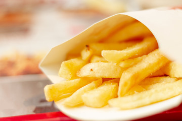 Yellow appetizing fried potato fries in a paper box closeup. Selective focus. Fast food in a cheap family restaurant.