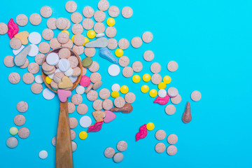 Assorted pharmaceutical medicine pills, tablets and capsules on wooden spoon on blue background.