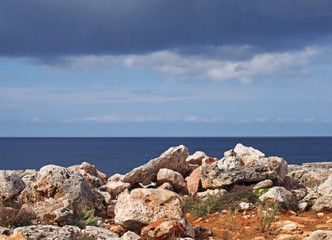 a rocky coastline scene with white stones against a calm blue sea and sky with sunlight and clouds