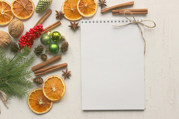 Christmas card, white paper notebook background surrounded by Christmas balls, fir branches, cinnamon sticks, spices, dried orange, wooden deer . Copy space.