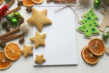 Christmas card, a blank sheet of paper and gingerbread surrounded by Christmas balls, fir branches, cinnamon sticks, spices, dried orange, wooden deer . Copy space.
