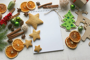 Christmas card, a blank sheet of paper and gingerbread surrounded by Christmas balls, fir branches, cinnamon sticks, spices, dried orange, wooden deer . Copy space.