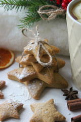 Obraz na płótnie Canvas A Cup of tea with lemon on the table close-up surrounded by Christmas decorations and homemade cakes. Star shaped gingerbread, cinnamon sticks and dried oranges on white background.