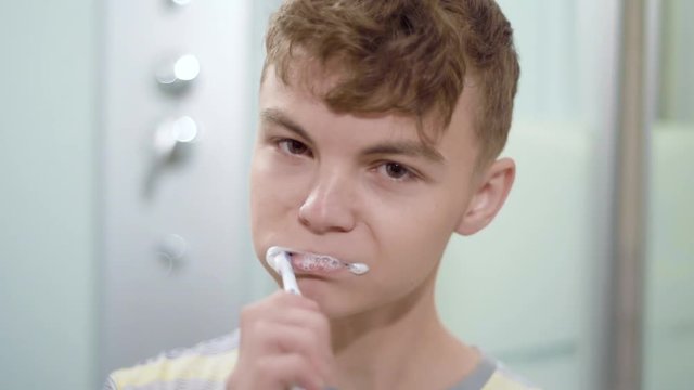 Morning in the bathroom. Teen boy brushing his teeth and looking at camera. Child takes care of health. 