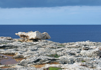a balanced boulder on a rocky coastline scene with white stones against a calm blue sea and sky...