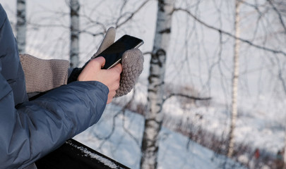 Close-up woman's hands in mittens writing messages on cellphone in winter park.