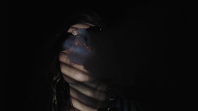 Vape woman. a handsome young white girl vaping and letting off puffs of steam from an electronic cigarette in dark room