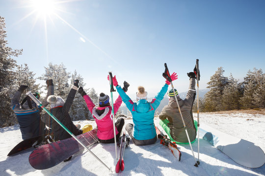 Skiers sitting on snow with hands up and resting, back view
