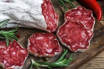 French salami with rosemary, chili pepper and peppercorns on wooden cutting board over rustic background