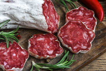 French salami with rosemary, chili pepper and peppercorns on wooden cutting board over rustic background