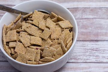 Breakfast cereal in white bowl with frozen blueberries and wood table background