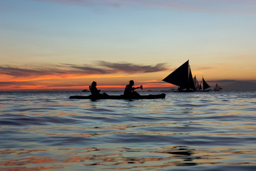  man and woman on the kayak on the background of yachts at sunset