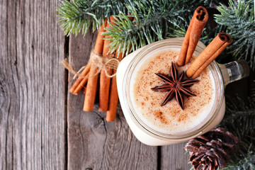 Christmas spiced eggnog in a mason jar. Above view with tree branches on a rustic wood background.