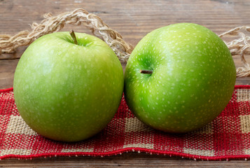 Pair of organic Granny Smith apples on red-checked burlap.