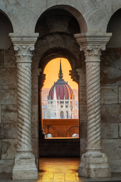 Budapest, Hungary - Golden sunrise at the Hungarian Parliament seeing through a medieval balcony with arch and gothic coloums