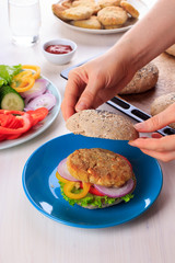 Cooking healthy vegan burger with chickpea fritters, vegetables and whole-wheat bun with sesame and poppy seeds on white table for breakfast