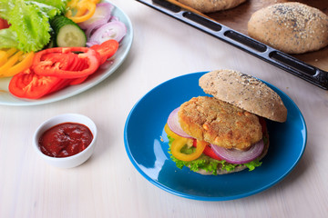 Healthy vegan burger with chickpea fritters, vegetables and whole-wheat bun with sesame and poppy seeds on white table for breakfast. Cooking, recipe