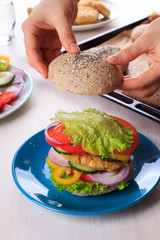 Cooking healthy vegan burger with chickpea fritters, vegetables and whole-wheat bun with sesame and poppy seeds on white table for breakfast