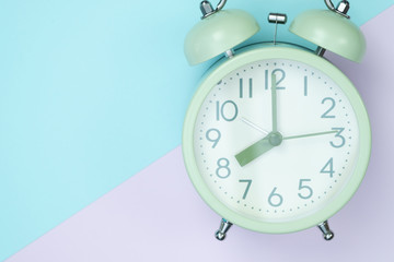 Vintage alarm clock on sweet pastel colored paper top view, background texture, pink, purple, yellow, beige, green and blue colour.