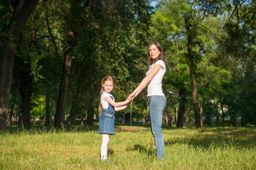 Naklejka na ściany i meble Mom and daughter stand on the lawn and hold hands
