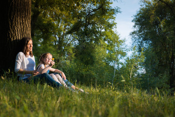 Naklejka na ściany i meble Mom and daughter are sitting near a tree